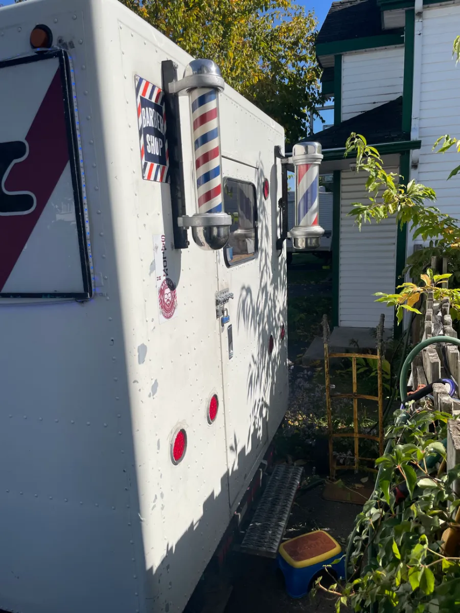 Le côté du salon mobile, ses poteaux de barbier et l'enseigne Barber Shop