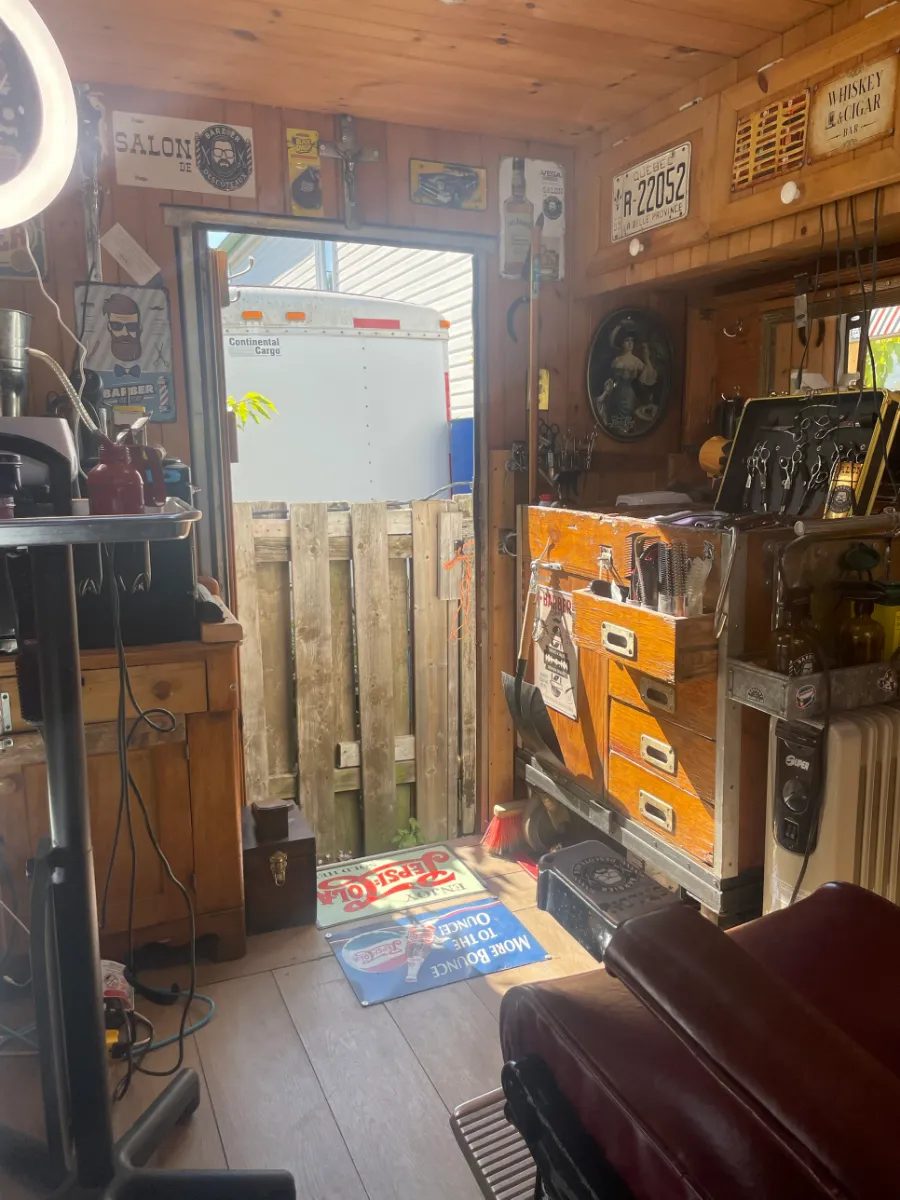 L'intérieur du salon vers la porte : coffre à outils en bois, ciseaux, plaques et affiches d'époque